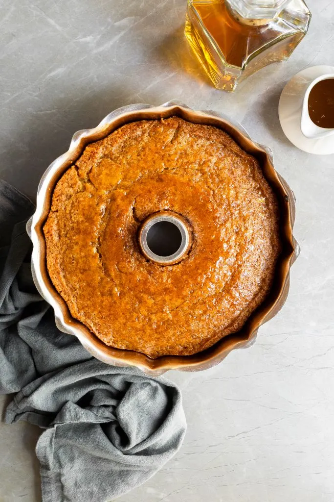 Top down view of rum cake cooling in bundt pan, with a small pitcher of rum sauce ready to apply to the cake