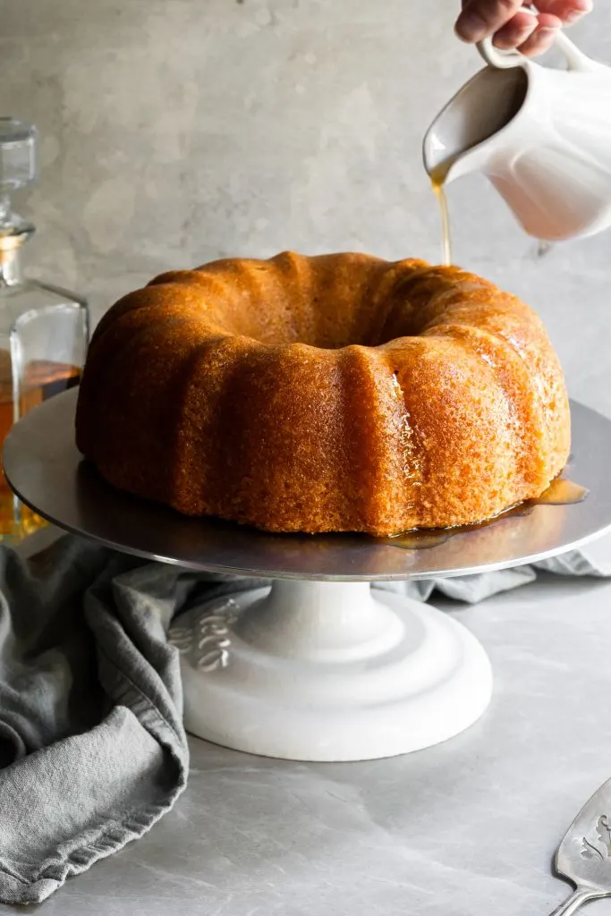 Vegan rum bundt cake on a cake stand and a stream of rum sauce being poured over the top
