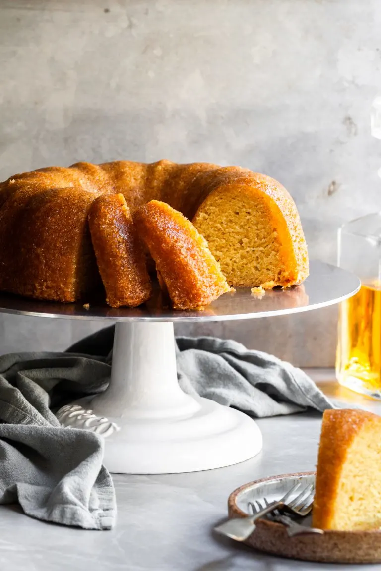 Sliced rum bundt cake on cake stand and a slice on a plate in the foreground