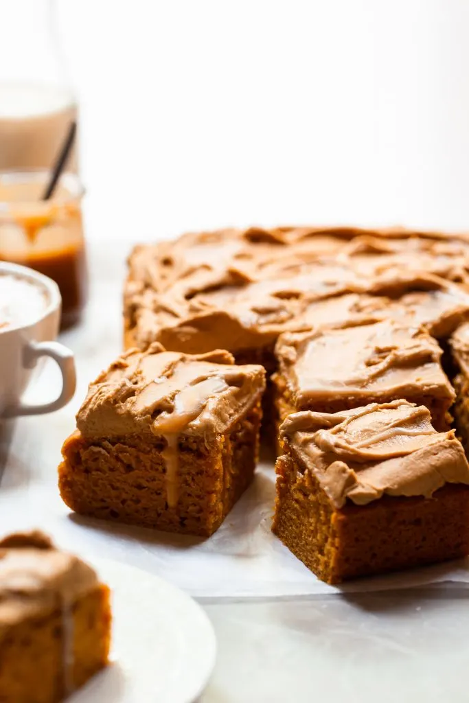 Sheet cake cut into square pieces, each covered in frosting and swirls of butterscotch, served with a pumpkin spice latte