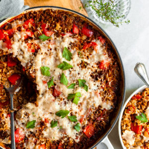 White skillet with a serving of pepper and rice casserole scopped out and served in a white bowl
