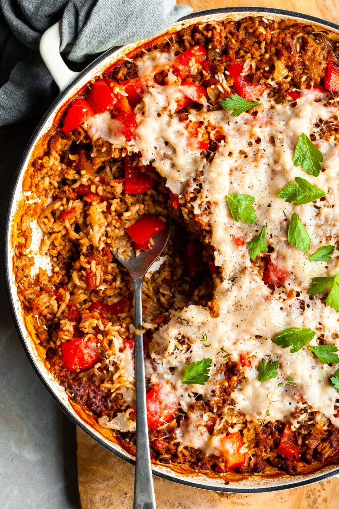 Close up of a white skillet with a serving of pepper and rice casserole scooped out