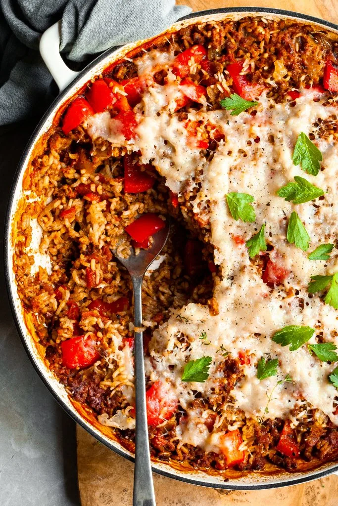 Close up of a white skillet with a serving of pepper and rice casserole scooped out