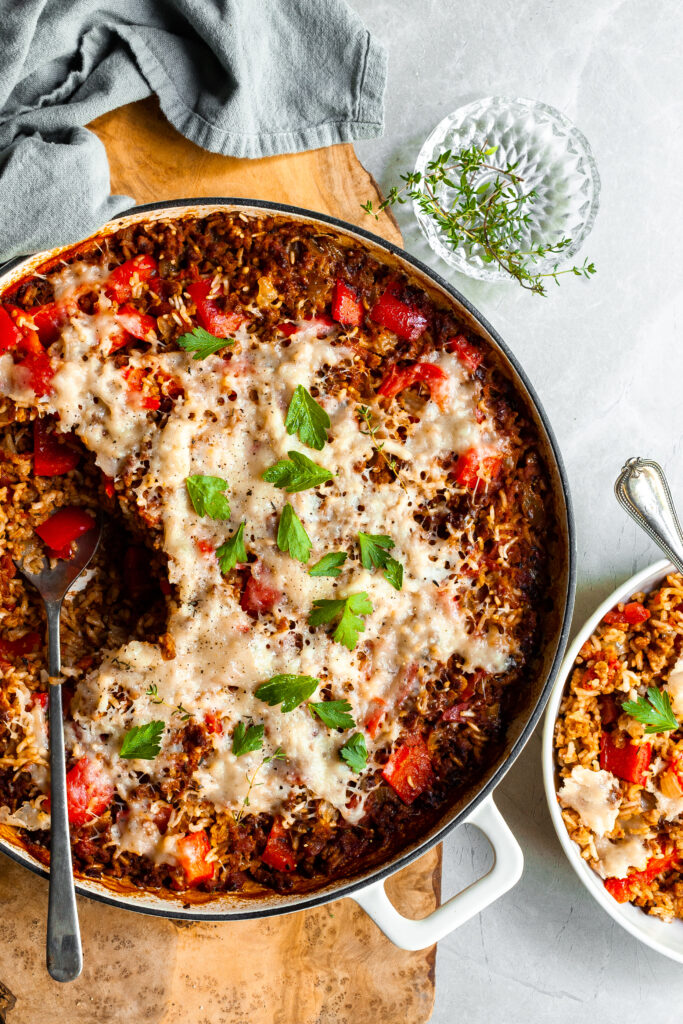 White skillet with a serving of pepper and rice casserole scopped out and served in a white bowl