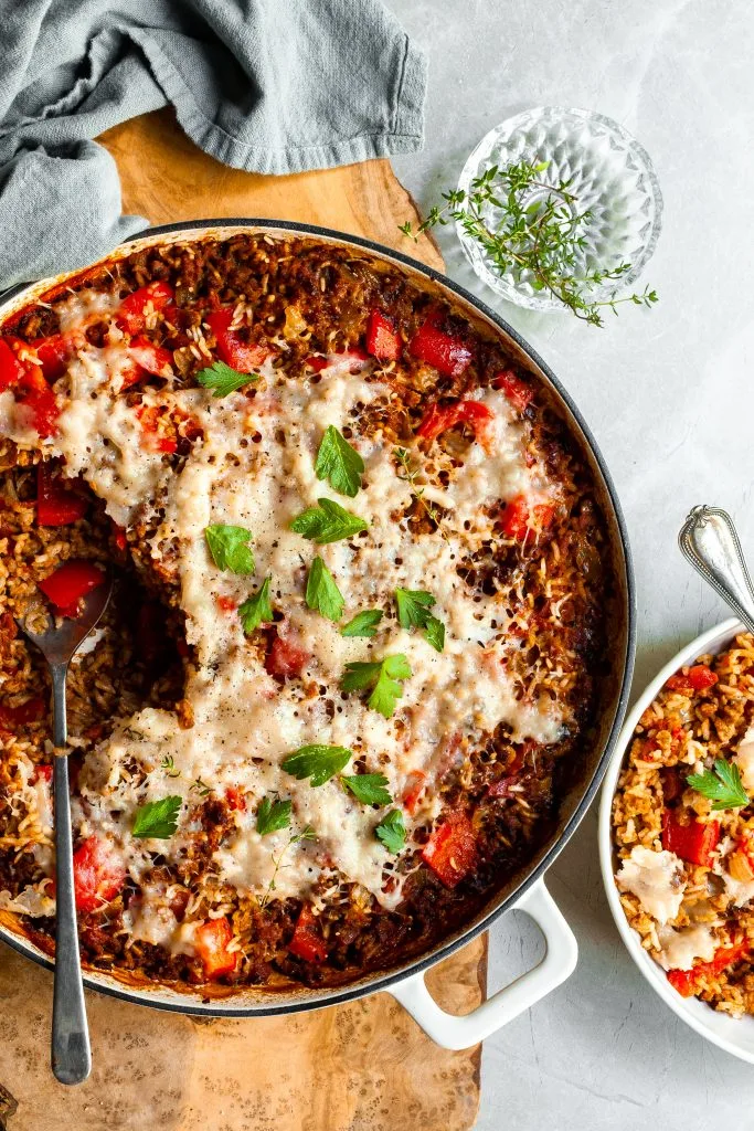 White skillet with a serving of pepper and rice casserole scopped out and served in a white bowl