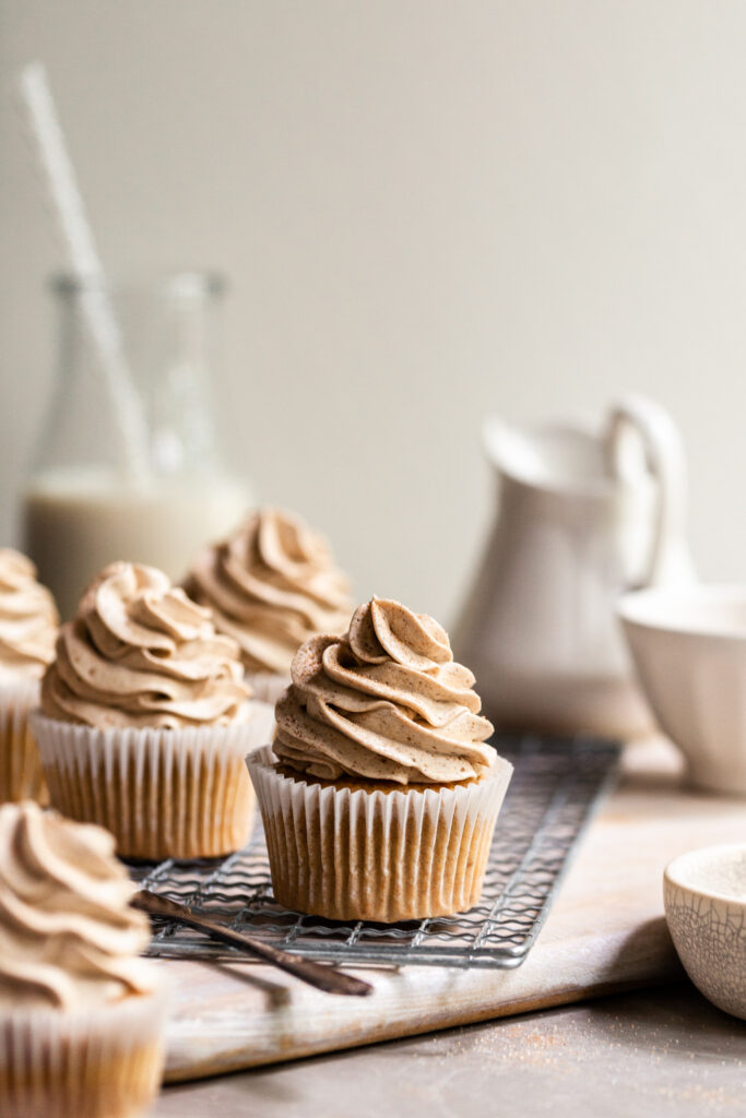 Frosted cupcakes on a cooling rack with a bottle of vegan milk in the background