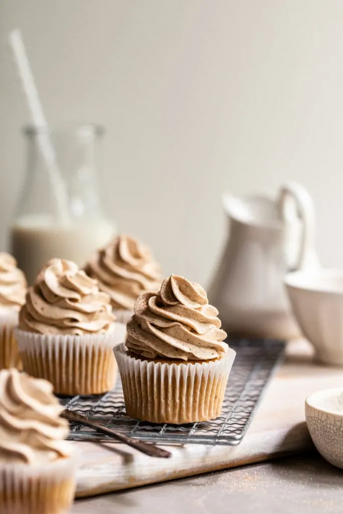 Frosted cupcakes on a cooling rack with a bottle of vegan milk in the background