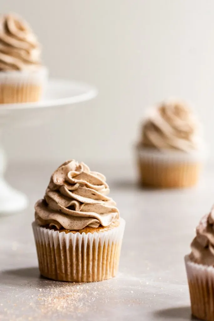 Vegan Banana Cupcakes with Cinnamon Ermine Frosting on a marble surface sprinkled with cinnamon sugar