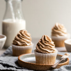 Vegan Banana Cupcakes with Ermine Frosting, one on a plate and 2 others in the background