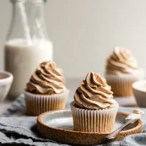 Vegan Banana Cupcakes with Ermine Frosting, one on a plate and 2 others in the background
