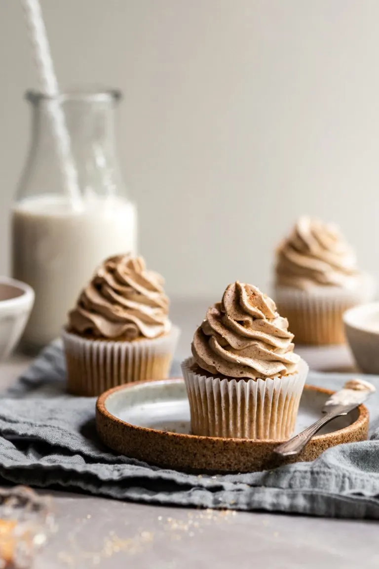 Vegan Banana Cupcakes with Ermine Frosting, one on a plate and 2 others in the background