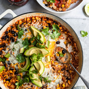 White skillet filled with rice, beans and corn with a serving just removed and spooned into a white bowl
