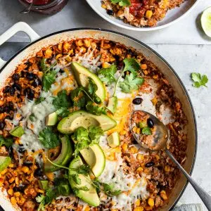 White skillet filled with rice, beans and corn with a serving just removed and spooned into a white bowl