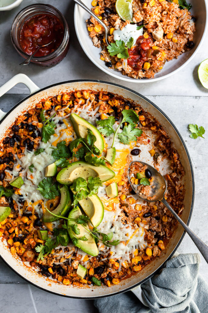 White skillet filled with rice, beans and corn with a serving just removed and spooned into a white bowl