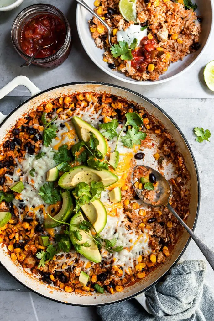 White skillet filled with rice, beans and corn with a serving just removed and spooned into a white bowl