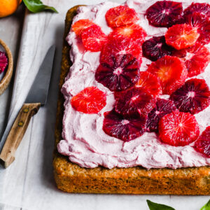 Angled side view of a sheet cake covered in pink frosting and slices of blood oranges