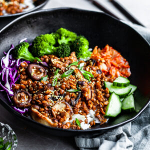 Angled view of a black bowl filled with rice topped with lentils, shiitakes, broccoli and kimchi