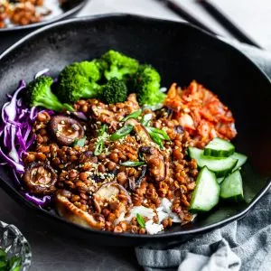 Angled view of a black bowl filled with rice topped with lentils, shiitakes, broccoli and kimchi