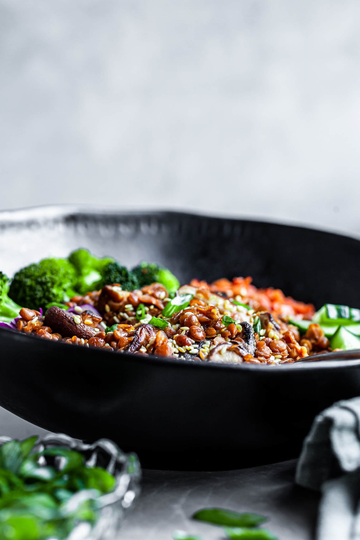 Peeking over a black bowl filled with rice, lentils, shiitakes, cucumbers, broccoli and kimchi