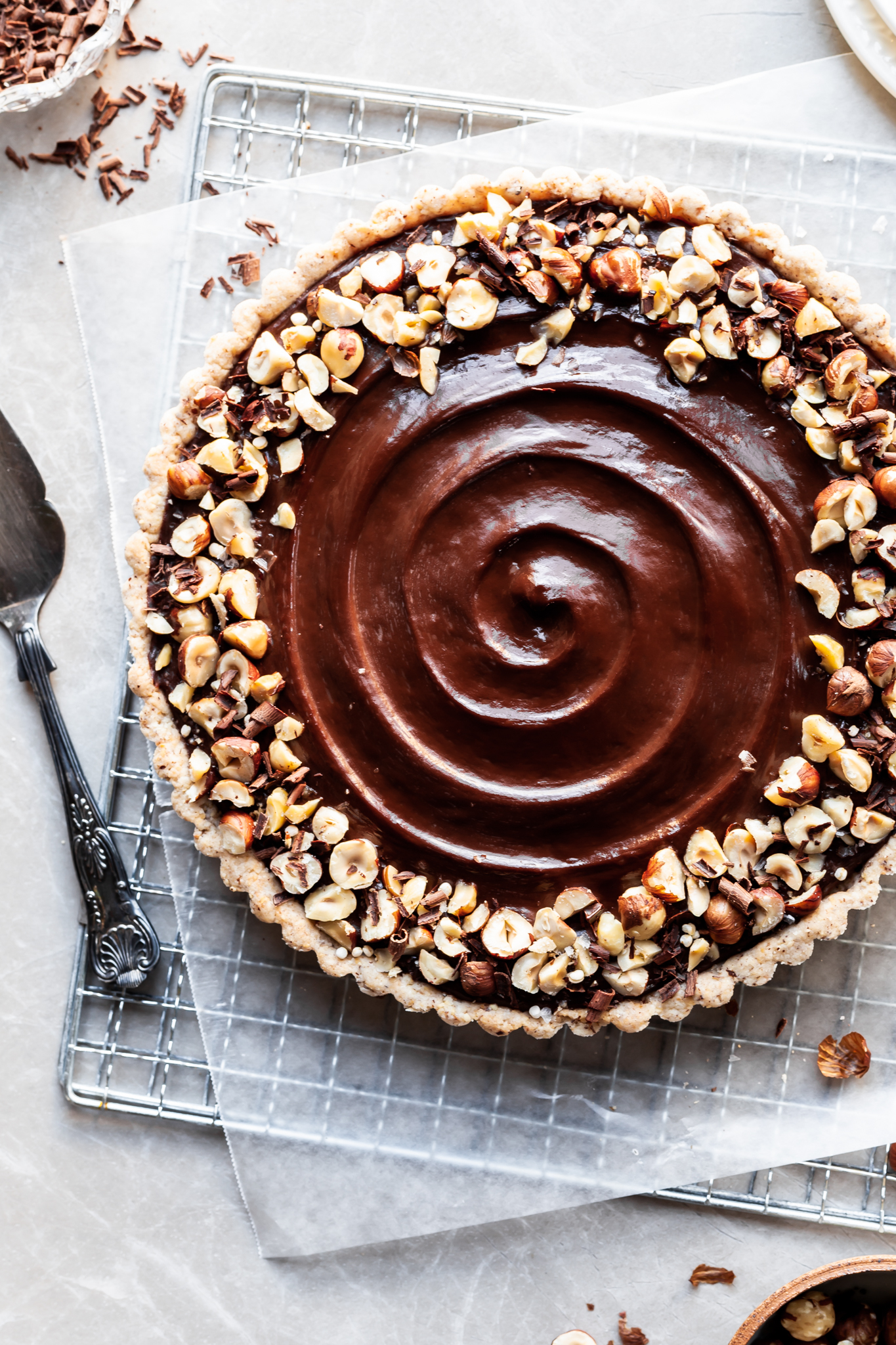 Cropped flatlay of a chocolate hazelnut tart so 1/8 of the tart is not visible. Beside the tart is an antique serving spatula 