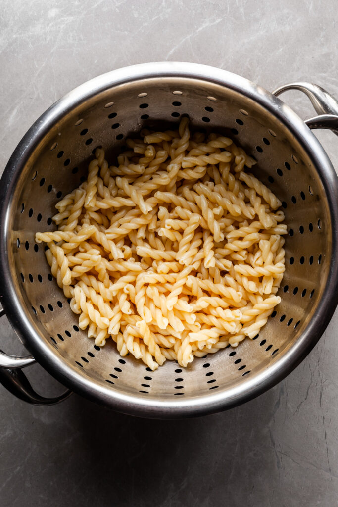 Flat lay of cooked gemelli pasta noodles in a stainless steel strainer