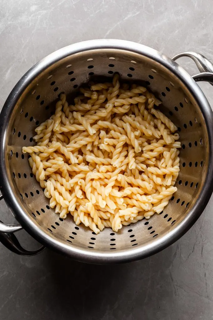 Flat lay of cooked gemelli pasta noodles in a stainless steel strainer
