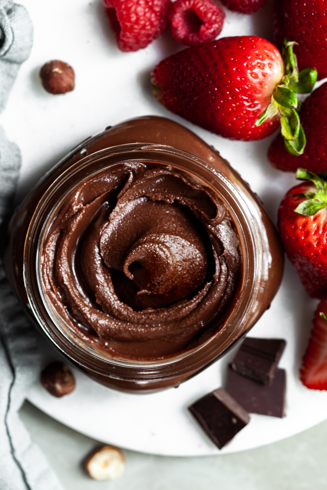 View into the top of a jar filled with chocolate hazelnut spread, sitting beside some strawberries