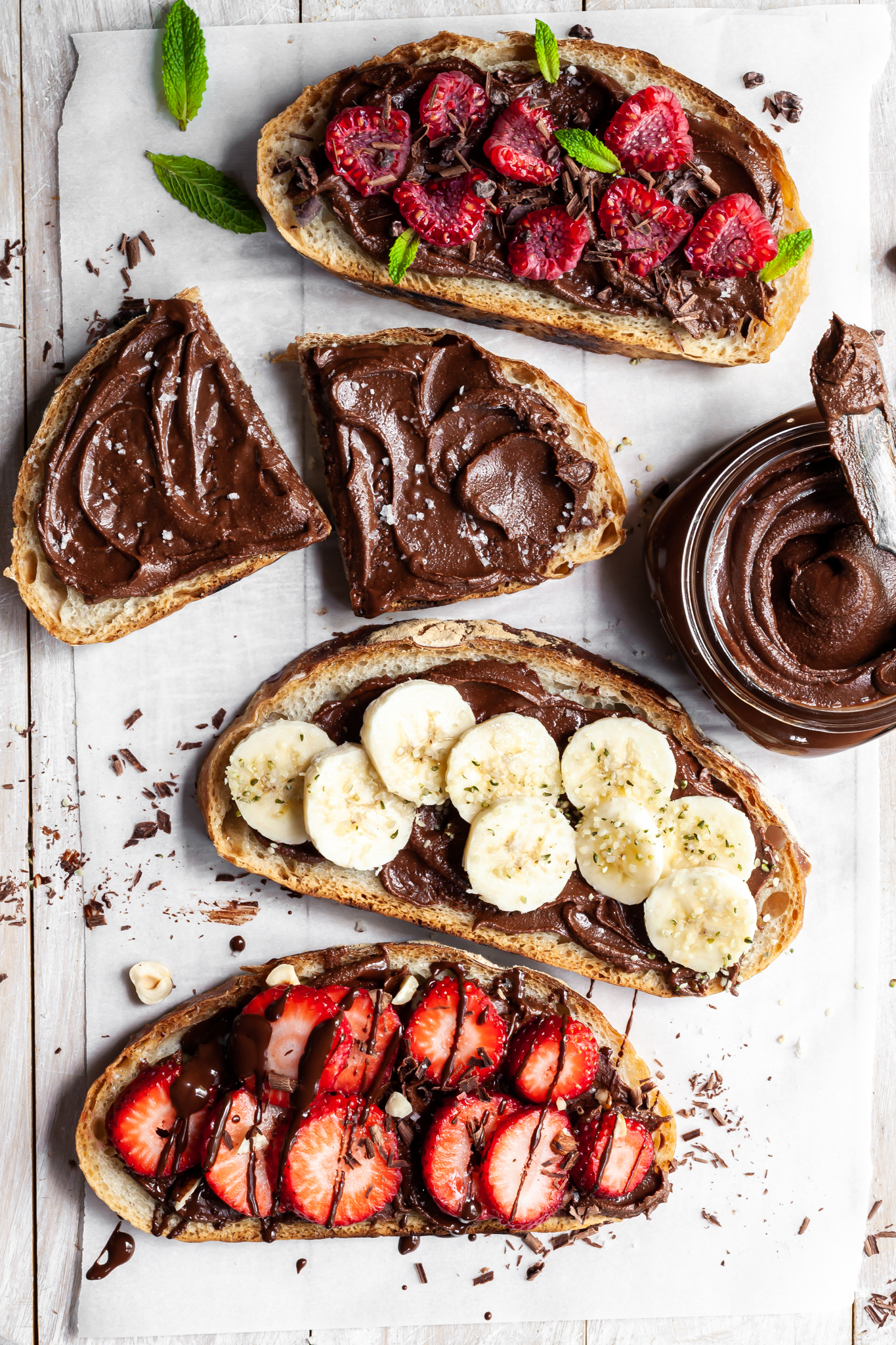 4 slices of bread covered in chocolate spread, one with banana slices, one with raspberries and one with strawberries