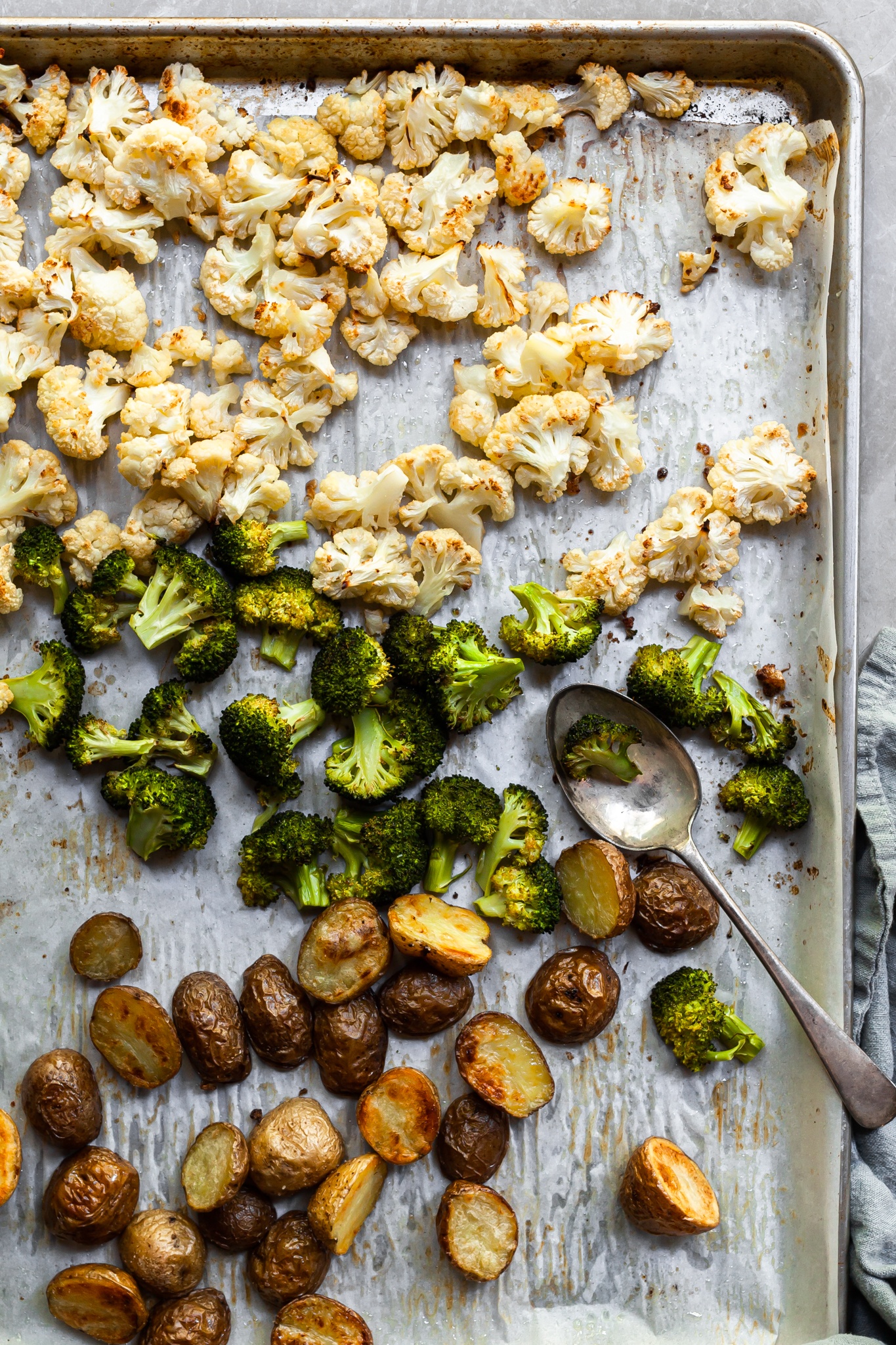 Baking tray lined with parchment paper in covered in roasted vegetables including baby potatoes, cauliflower and broccoli 
