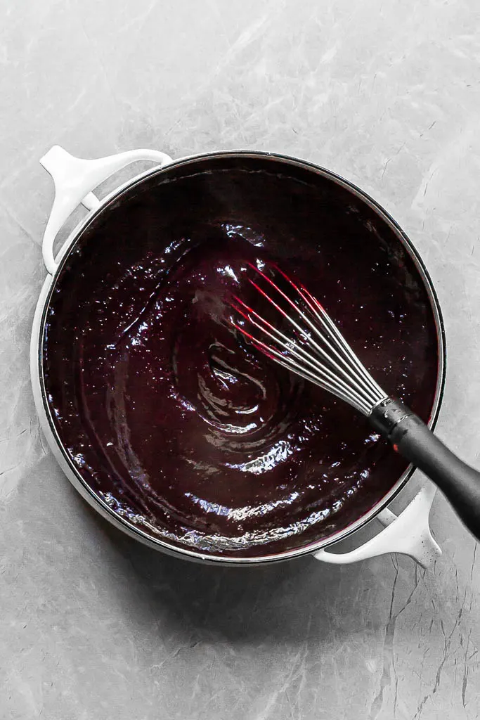 Deep purple berry curd in a white pot after the seeds have been strained out so the mixture is smooth and thick.
