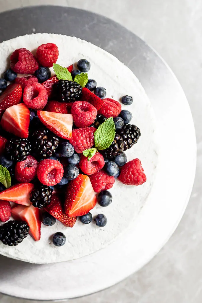 View top down of a round vanilla frosted cake covered in raspberries, blueberries, blackberries and strawberries. 