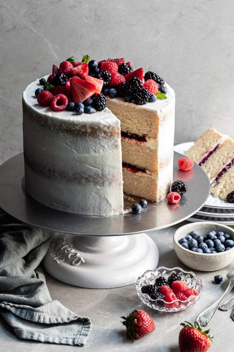 Triple layer vanilla cake layered with fruit filling with a slice cut. A plate in the background with the cut slice of cake.