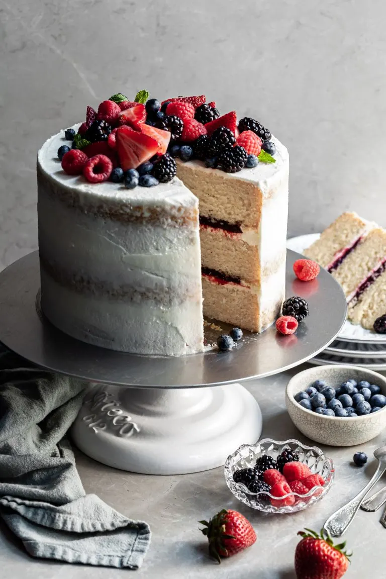 Triple layer vanilla cake layered with fruit filling with a slice cut. A plate in the background with the cut slice of cake.