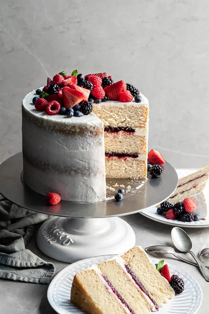 Vanilla berry layer cake with 2 slices cut resting on white plates, garnished with fresh berries.
