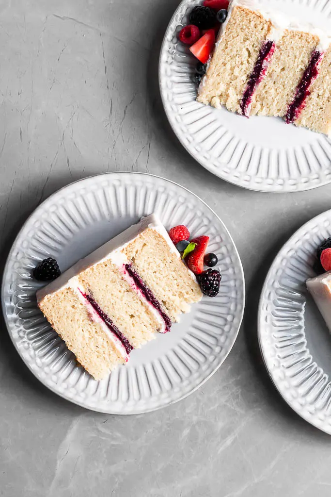View looking down on 3 white plates on marble counter, each with a slice of berry vanilla cake.