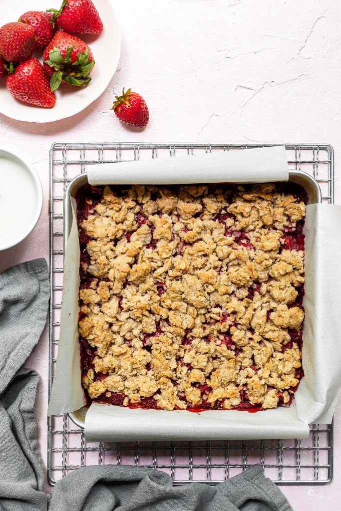 Square aluminium pan lined with parchment paper, filled with freshly baked strawberry crumb bars