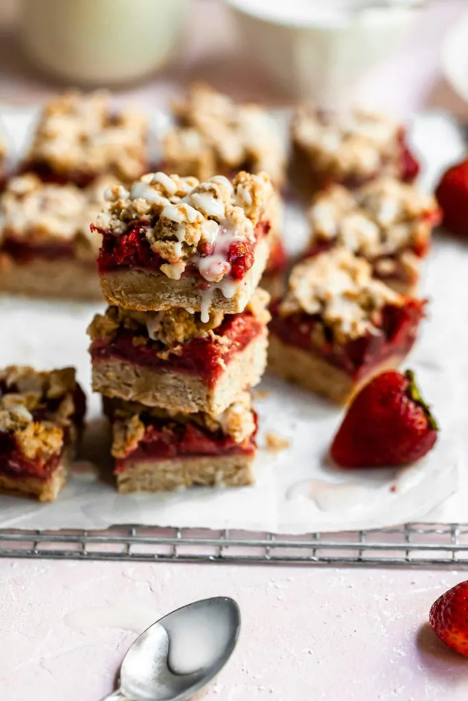 Stack of 3 strawberry crumble bars with fresh strawberries in the background