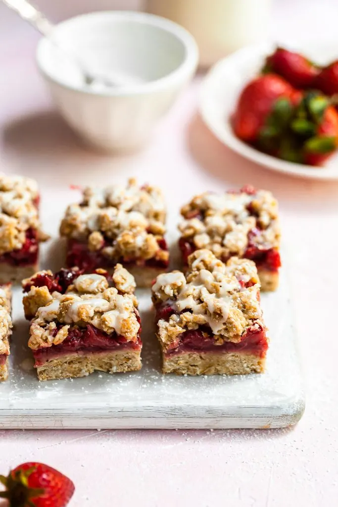 Close up of vegan strawberry crumb bars on a white cutting board, just drizzled with vanilla glaze