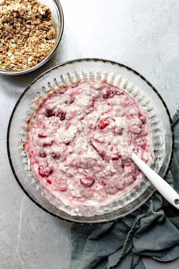 Bowl of strawberry muffin batter beside a bowl of oatmeal crumb topping