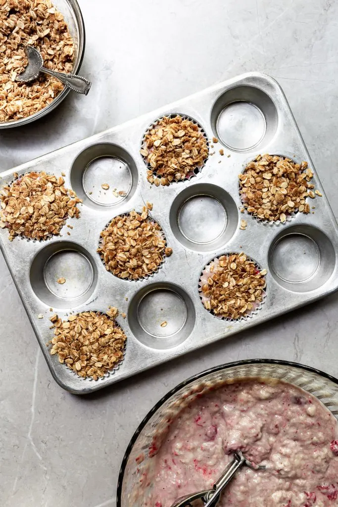 A muffin tin filled with batter and topped with oatmeal streusel, all ready for the oven