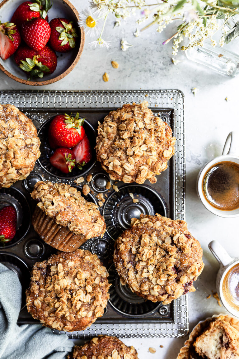 View looking down on a baking tray of muffins beside a bowl of strawberries, a vase of wildflowers and 2 some cups of espresso