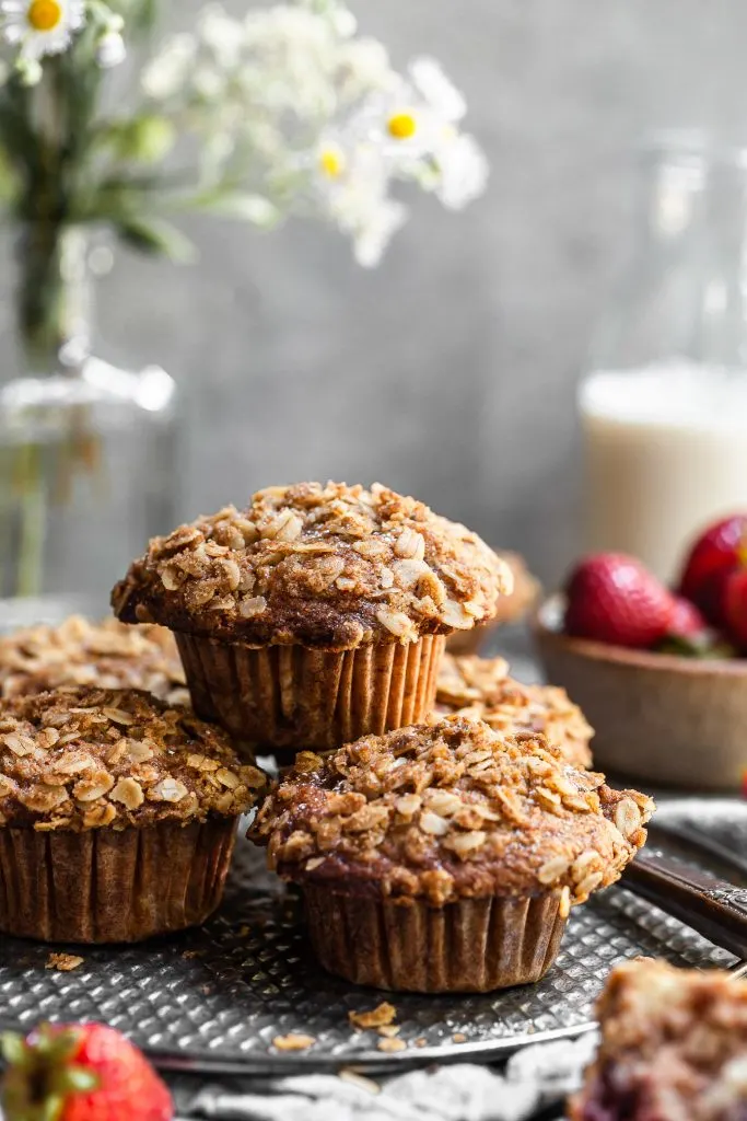 Fresh muffins stacked on an antique tray with a bottle of soy milk and a bowl of strawberries in the background