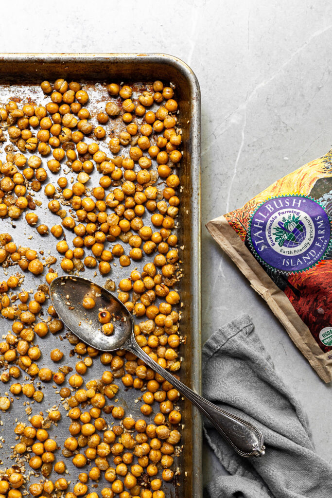 Baking tray filled with roasted chickpeas covered in sesame seeds