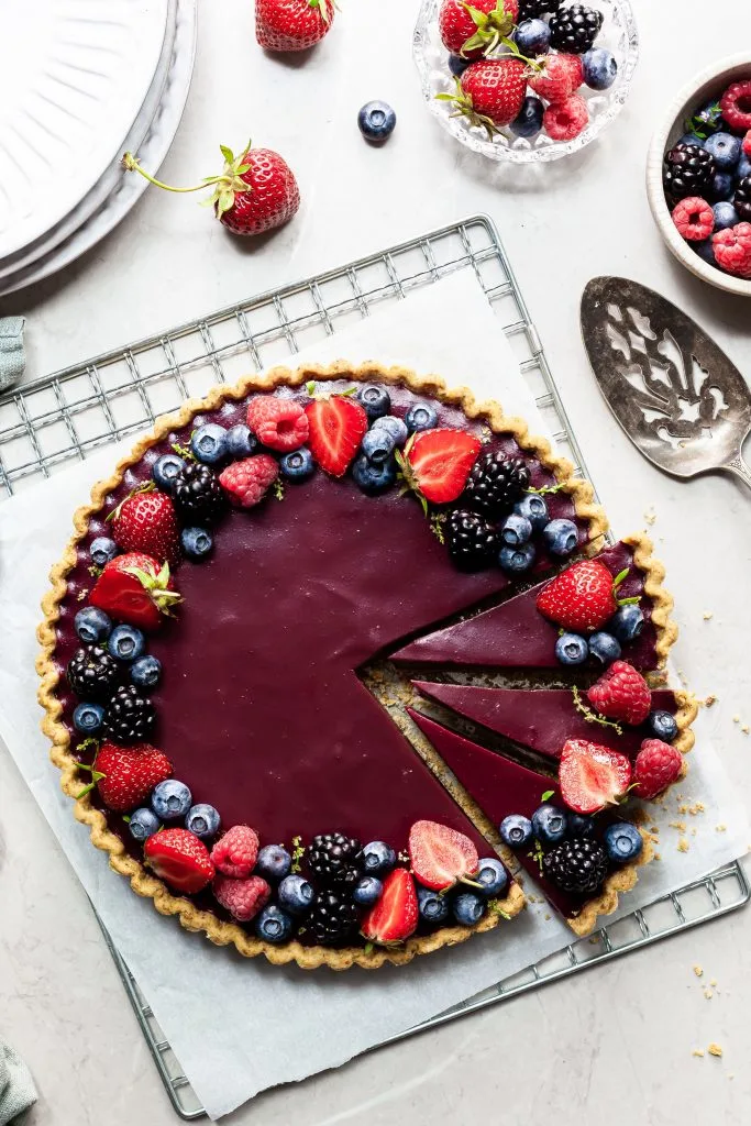 flatlay of a berry tart, the filling is purple and it's garnished with various summer berries