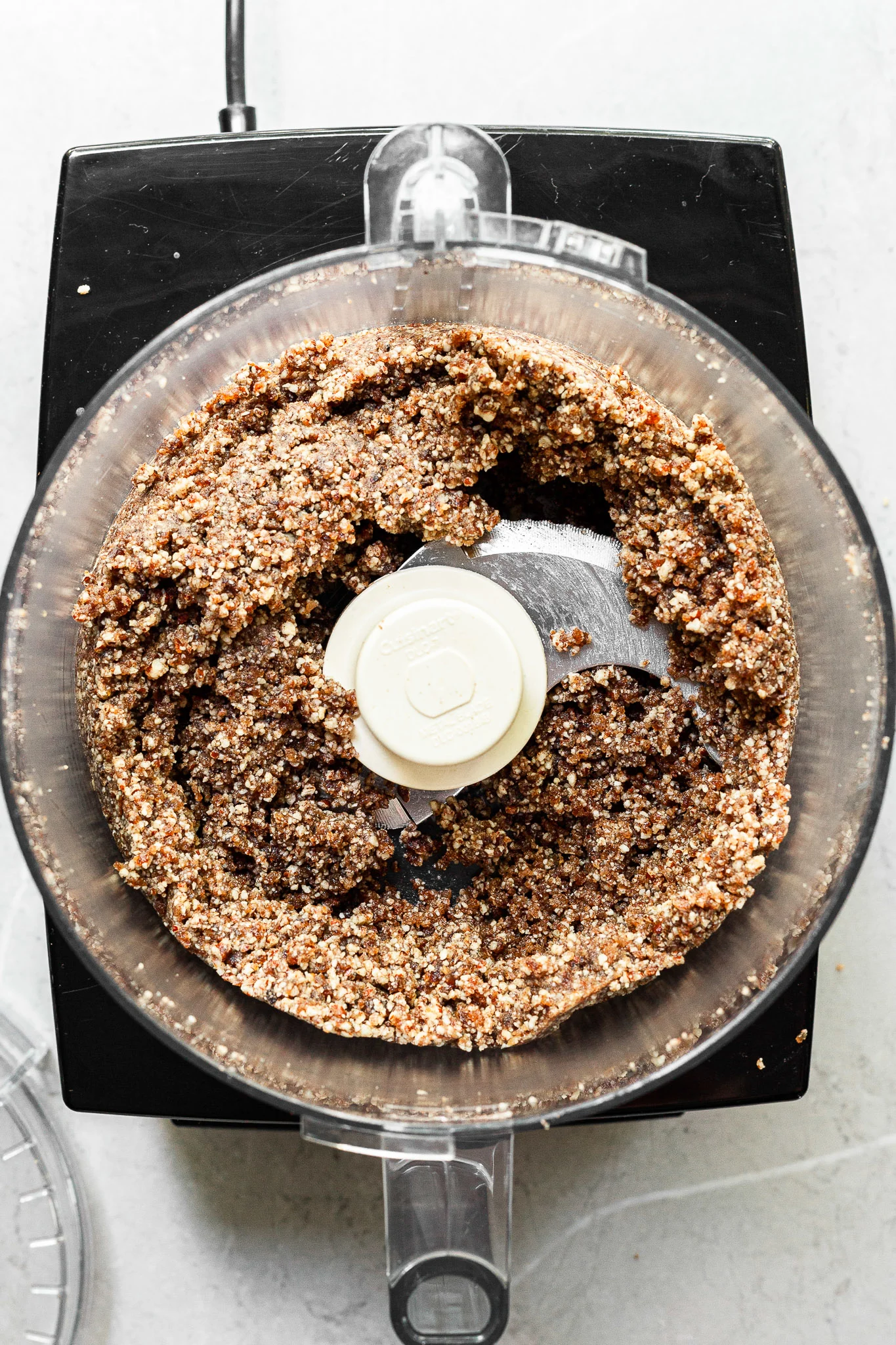 view into a food processor filled with blended up pecans and dates ready to be pressed into tart pans