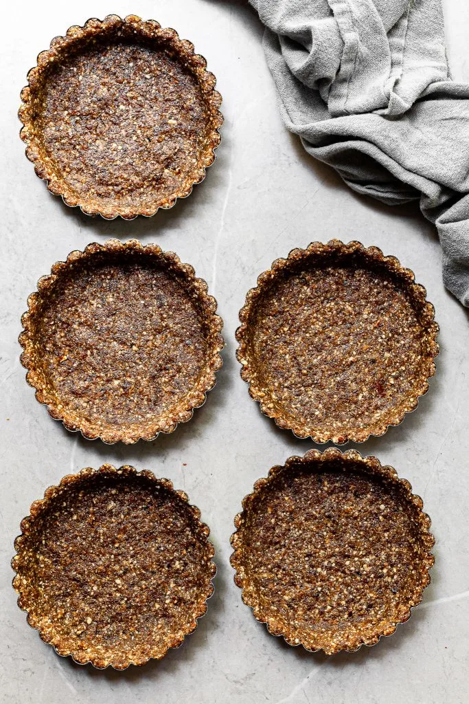 5 tart pans with the no-bake pecan date crust pressed into them