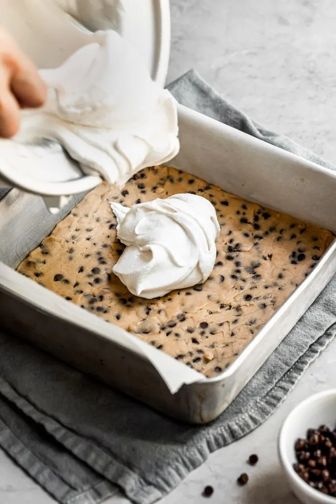 creamy vanilla ice cream with the consistency of soft serve being scooped onto a layer of cookie dough in a square aluminum baking pan