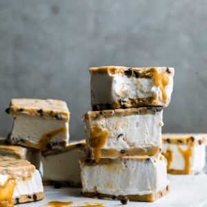 a stack of chocolate chip cookie dough ice cream sandwiches dripping with caramel