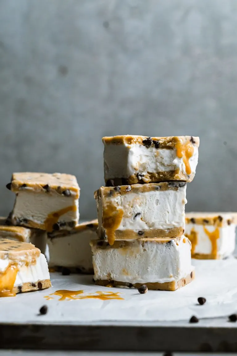 a stack of chocolate chip cookie dough ice cream sandwiches dripping with caramel