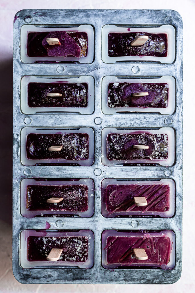 View looking down on popsicle mold straight out of the freezer containing purple popsicles with flecks of ice and frost on the surface